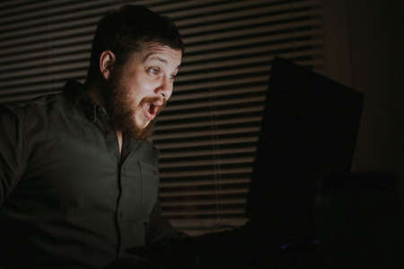 Surprised guy reading news by laptop in evening.の写真素材