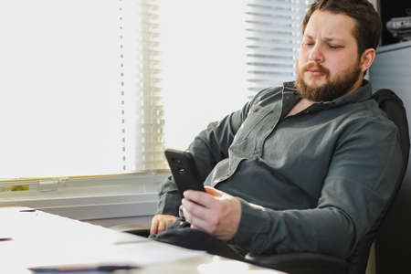 Successful business director sitting and using smartphone in office.の写真素材