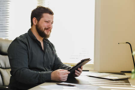 Male employee using tablet at office, laptop on desk.の写真素材