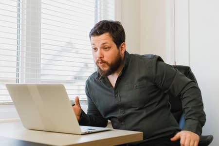 Successful businessman sitting at office with laptop near window.の写真素材