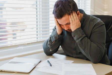 Sad thinking caucasian manager working with documents at office, closed laptop on desk.の写真素材