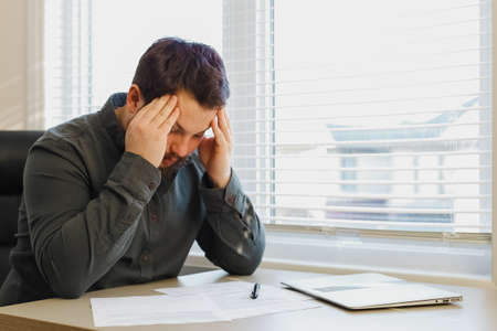 Sad thinking marketolog working with documents at office, closed laptop on desk.の写真素材