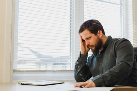 Tired thinking enterpreneur working with documents at office, closed laptop on desk.の写真素材