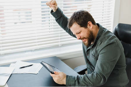 Gladden businessman enjoying success and using tablet at office.の写真素材