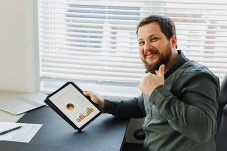 Successful businessman showing thums up and using tablet with graphs.の写真素材