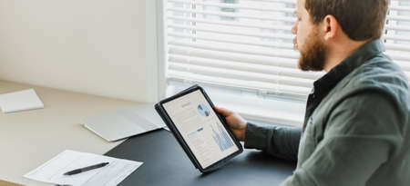 Adult businessman sitting at desk with tabet, graphs on screen.の写真素材