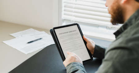 Man reading partnership agreement on tablet.の写真素材