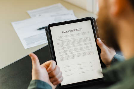 Man signing sale contract on tablet and showing thumbs up.の写真素材