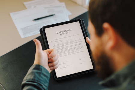 Male person reading car selling contract on tablet and showing thumbs up.の写真素材