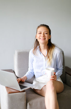 Young smiling woman working with laptop at home and drinking coffee.の写真素材