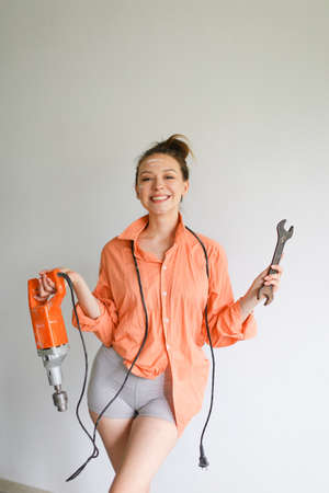 Young happy girl holding a drill and wrench, wearing orange shirt standing on isolated background.の写真素材