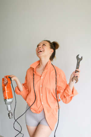 Young smiling girl holding a drill and wrench, wearing orange shirt standing on isolated background.の写真素材