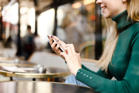 Blonde girl chatting by smartphne and sitting at street cafe.
