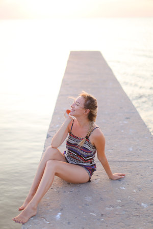 Young european woman sitting on pier and wearing swimsuit.の写真素材
