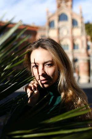 Portrait of caucasian pretty girl with palm leaf, old building in background.の写真素材