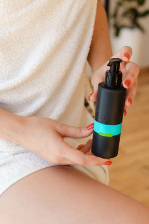 Beautiful fresh young woman applying cream or body wash on hand from dispenser indoorsの写真素材