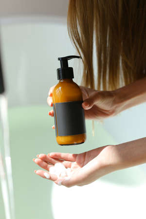 Woman holding bottle with spa cosmetics in bathroom. Beauty blogger, salon therapy, minimalism concept, copyspaceの写真素材