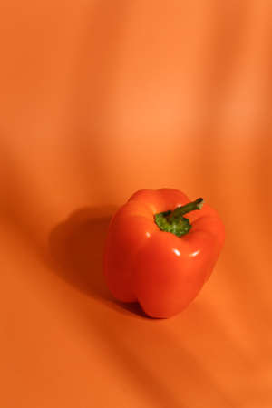 Fresh sweet orange pepper isolated on neutral orange background closeup