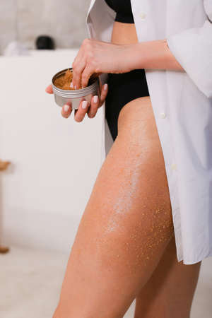 Woman applying nourishing scrub on body on bathroom background, closeupの写真素材
