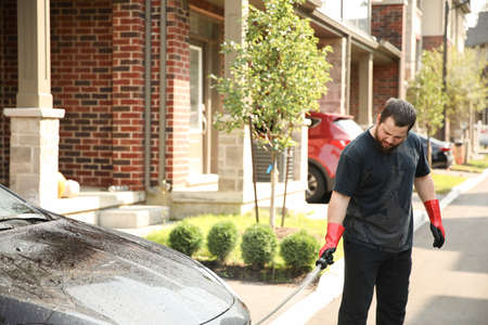 European man washing car by water and jet in front of house.