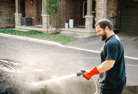 Cacuasian man washing car by water jet in front of house at home.の写真素材
