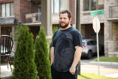 Young man watering plants and looking at camera in front of house.の写真素材