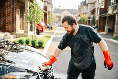 American Man washing own black car outside with sponge and wearing red gloves looking at carの写真素材