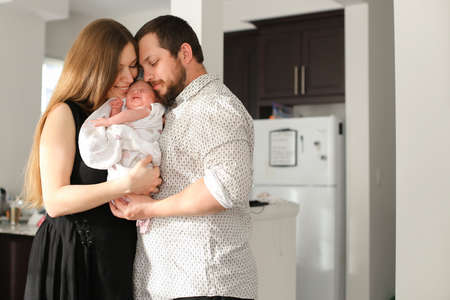 Portrait of young parents holding and hugging little female baby in flat.の写真素材