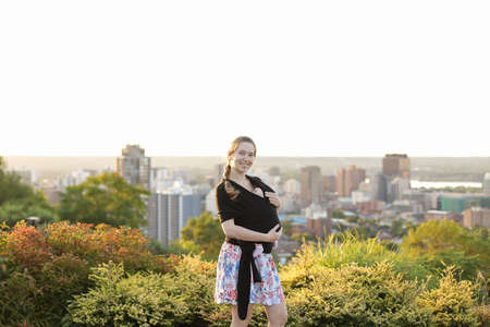 Caucasian mother carrying babe in sling city in background.の写真素材