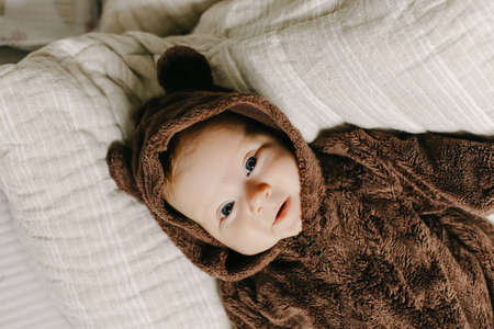 Newborn baby lying on back on white bedspread and wearing bear suit.の写真素材