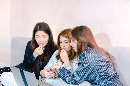 Friendly female friends cool spend time watching movies on laptop and sitting on soft sofa in bright bedroom in evening.の写真素材
