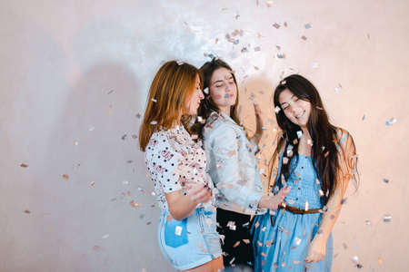 Funny girls pose in camera with smiles on their faces and stand against background of light wall in room.の写真素材