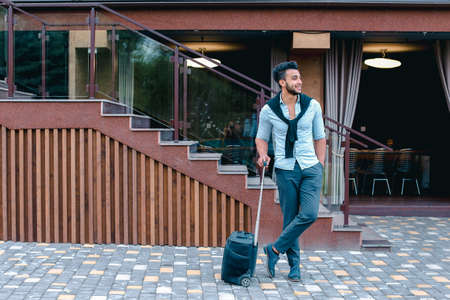 Young Guy Arab Businessman Student Came go to Restaurant With Suitcase in Hand, Smiling at Camera, Stops and Looks Away.の写真素材