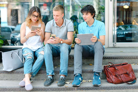 Young three friends sitting floor in the street, talking, usingの写真素材