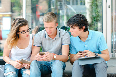 Young three friends sitting floor in the street, talking, usingの写真素材