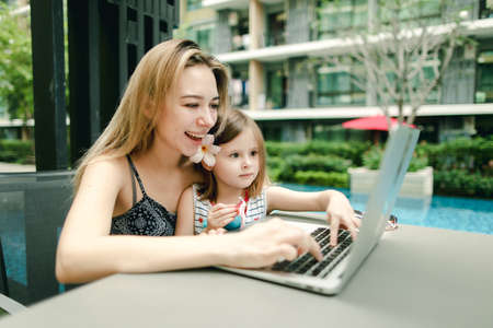 mother and daughter use laptop on background of swimming pool onの写真素材