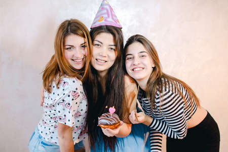 Lovely friendly girls celebrate birthday of their female friends and have fun standing on background of light wall in room.の写真素材