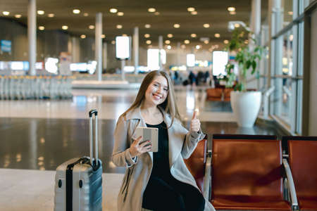 Woman using internet by tablet in airport hall near valise and sの写真素材