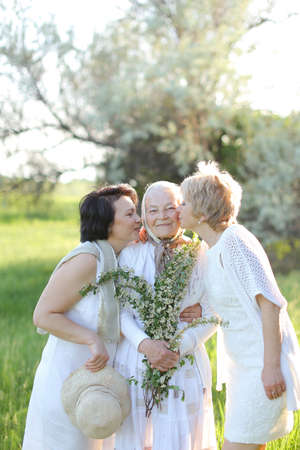 Two happy daughters kissing old mother outside and wearing white dresses.の写真素材