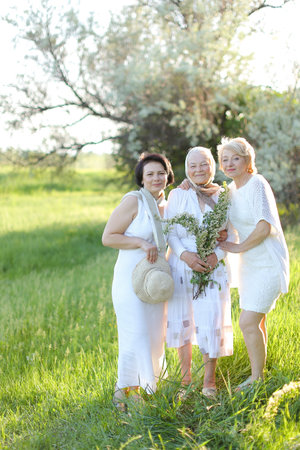 Two daughters standing with old mother outside and wearing white dresses.の写真素材