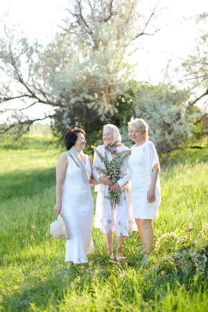 Happy daughters standing with old mother outside and wearing white dresses.の写真素材