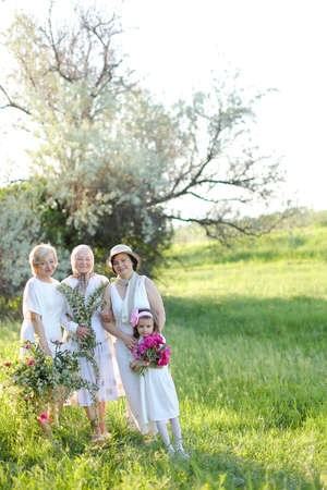 Caucasian happy grandmother in white dress with daughters and granddaughter outside.の写真素材