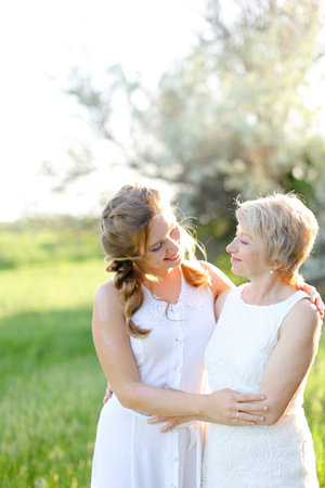 Portrait of girl standing with mother outside and wearing white dress.の写真素材
