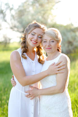 Portrait of caucasian girl hugging mother outside and wearing white dress.の写真素材
