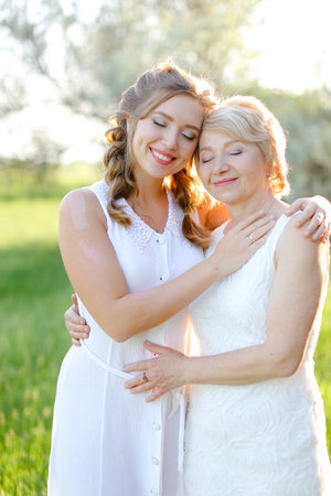 Portrait of girl hugging mother outside and wearing white dress.の写真素材