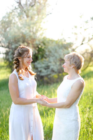 American girl holding mother hands outside and wearing white dress.の写真素材