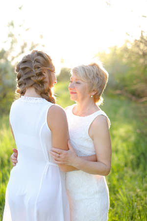 Blonde mother hugging back view daughter and wearing white dress.の写真素材