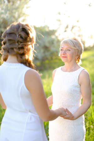 Blonde mother holding back view daughter hands and wearing white dress.の写真素材