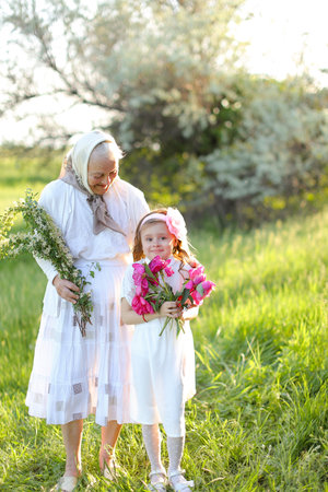 Old european granny standing with little granddaughter and keeping flowers.の写真素材