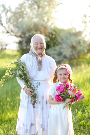 Old smiling granny standing with little granddaughter and keeping flowers.の写真素材
